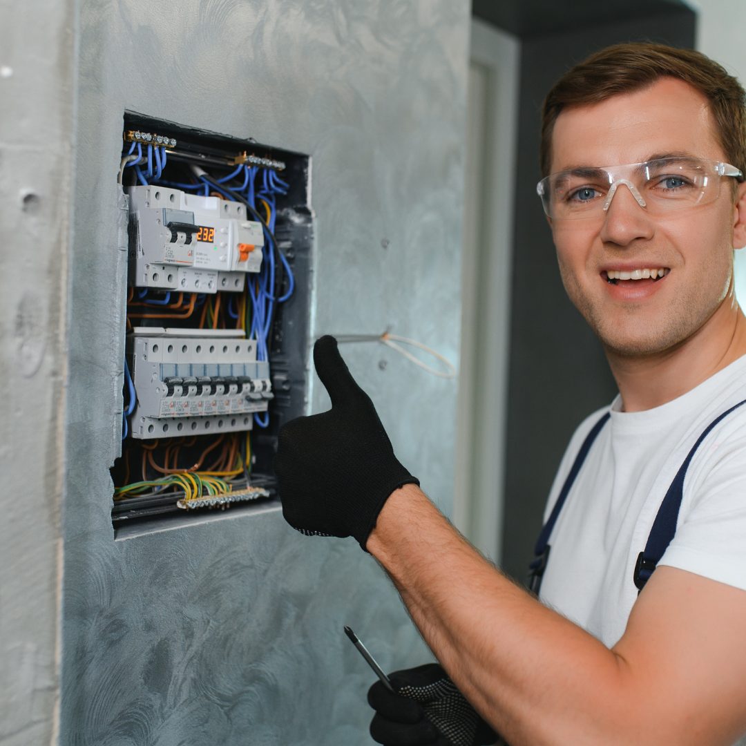 Residential electrician giving a thumbs-up while working on a circuit panel.